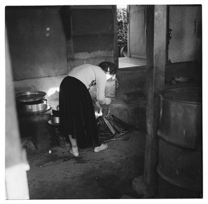 Woman bending over a kettle insdie her house, Korea