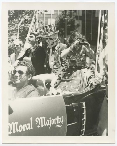 Costumed parade goers ride in car with sign reading "Moral Majority"