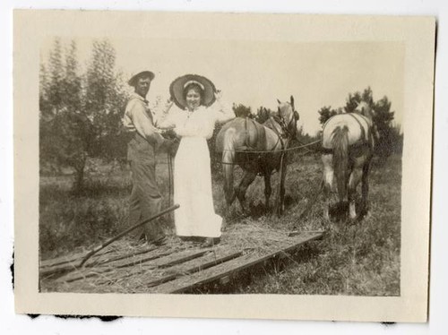 Man and woman riding a hay sled pulled by horses