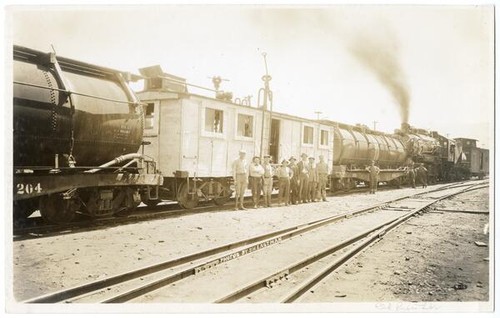 Unidentified men standing in in front of railroad cars, California