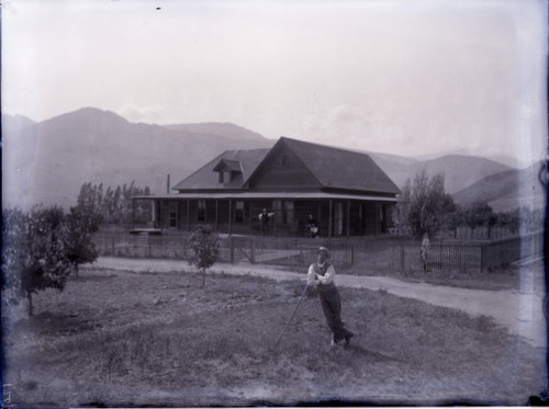 Man with rifle(?) in front of house