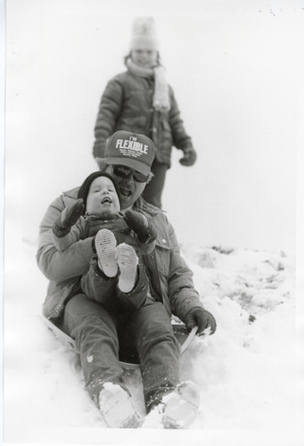 Father and Son Sliding Downhill on Snow