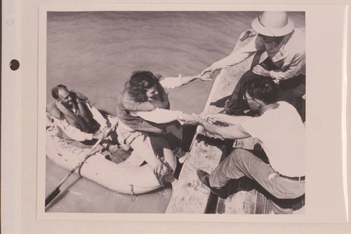 Georgie White being pulled aboard the Park boat. Harry Aleson sits at oars in the one-man raft. The two started at Parashont Wash and swam and rode down the river until met above Emory Falls 1946, June 30