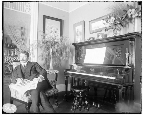 A man sitting in a chair by the Fischer piano in a house