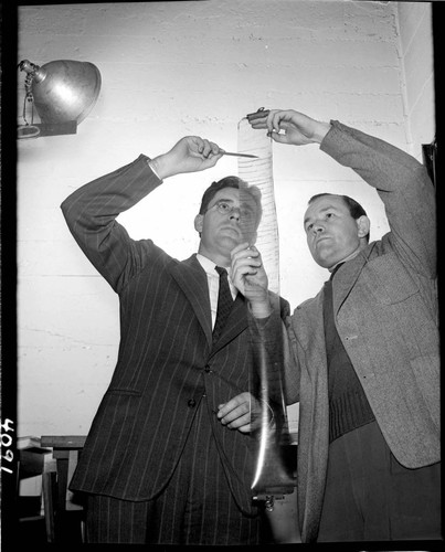 Two men looking at data plots on a roll of film they're holding up to the light