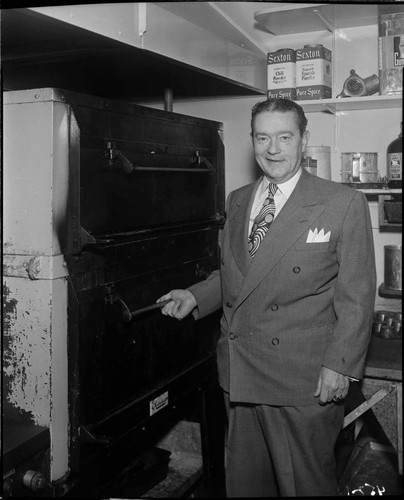 Man in suit standing next to commercial electric oven in restaurant kitchen