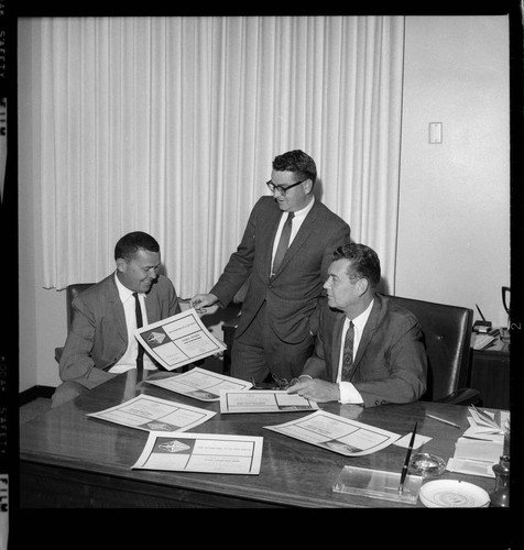 Three men at an office with award certificates