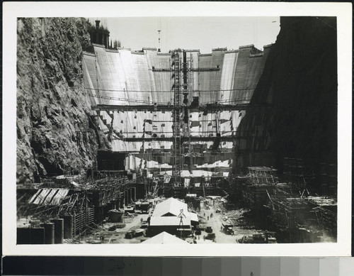 Downstream face of Hoover Dam during construction showing facilities under construction in the de-watered river section