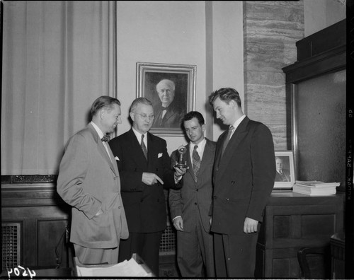 Four men in an office with a painting of Edison on the wall