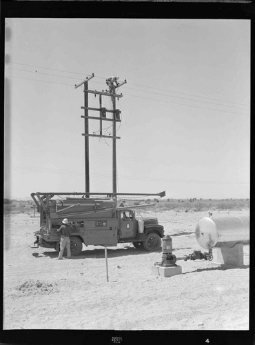 Linemen installing transformers on a pair of distribution poles in the desert