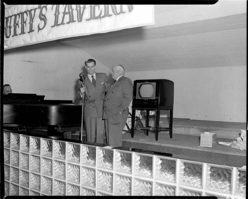 Two men standing at a microphone speaking with an RCA television behind them and a banner for "Duffy's Tavern" above them