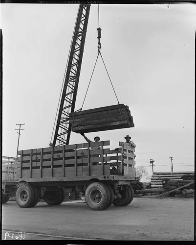 Crane loading or unloading wooden railroad ties from truck