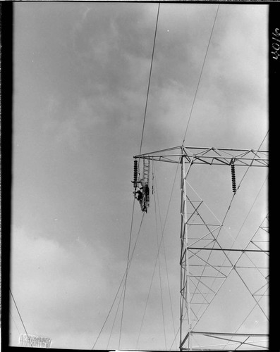 Men hanging from tower crossarm stringing conductor