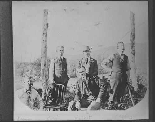 Five men outside posing for the picture with a dog sitting on a chair