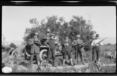 Five unknown men wearing suits and ties in the field with shotguns on an hunting trip