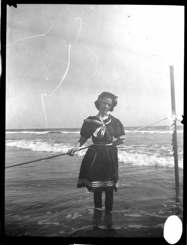 A young lady in a bathing dress wading in the water at the beach