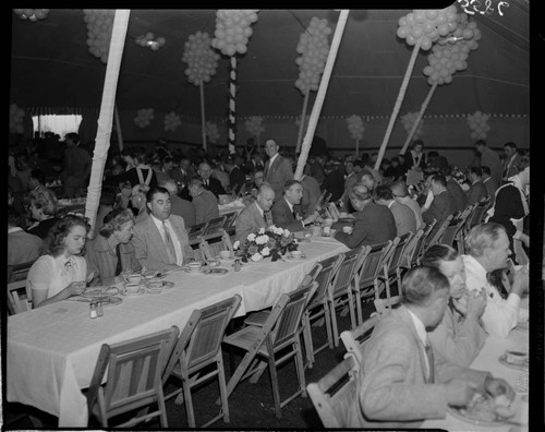 Large group of people eating long tables in a large tent