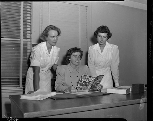 Three women looking at a cookbook for cooking electronically