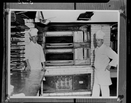 Two chefs standing by electric bake ovens in a commercial kitchen