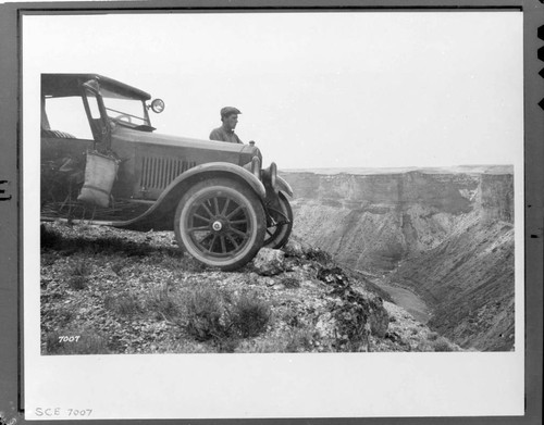 Man standing by 1920's automobile with water bag hanging on door at the edge of what is probably the Grand Canyon