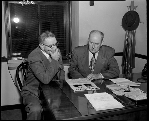 Two men at a desk looking over FBI wanted poster