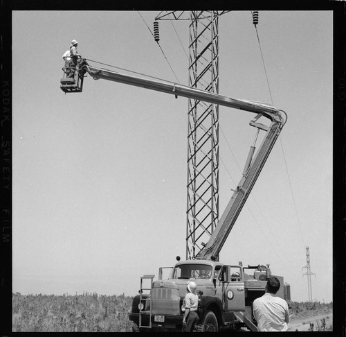 Raising bucket at tower with two men inspecting insulators