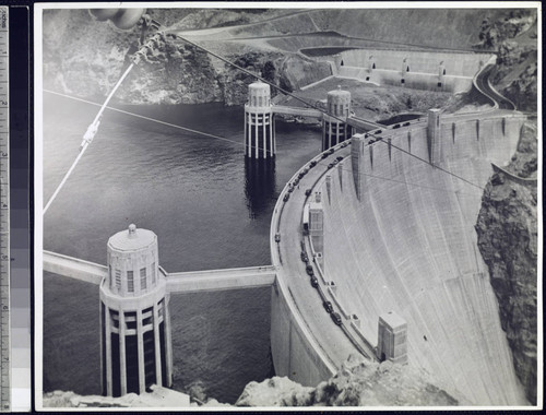 Hoover Dam from above showing completed dam with automobiles parked on road crossing dam