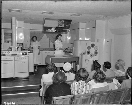 Two women demonstrating electric cooking techniques to audience