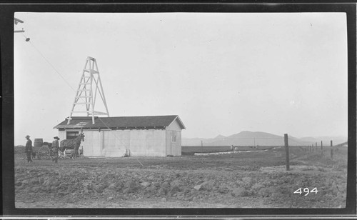 Two men and a horse-drawn cart standing outside a pumping plant in Tulare County
