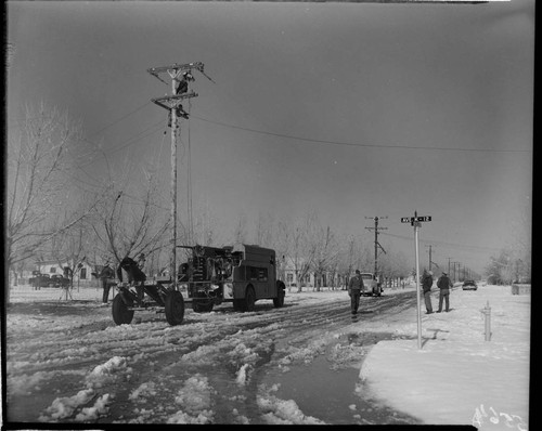 Linemen working on pole in snow at corner of Ave. K