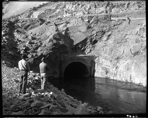 Dam 7 construction work: two men watching water flowing through diversion tunnel