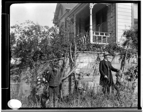 A man and two young boys standing by a wall below a residence