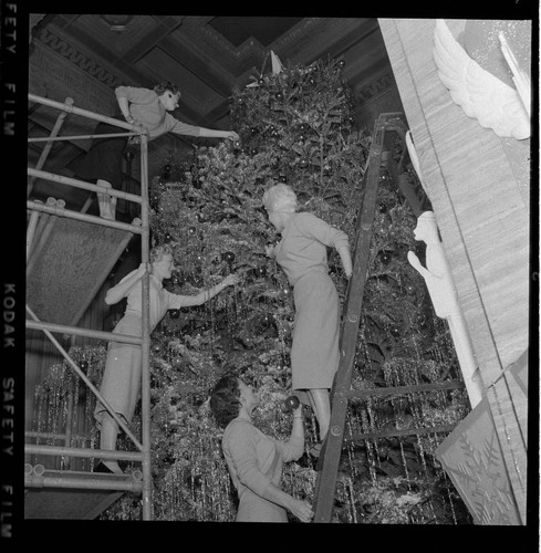 Four ladies on scaffolding and ladders decorating Christmas Tree in General Office lobby