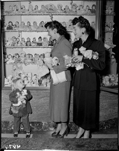 Two ladies and a little girl with two dolls at Christmas display