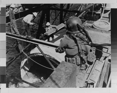 During construction of the Huntington Beach Steam Station in 1957, a deep sea diver prepares to descend to the ocean floor to guide a section of cooling water conduit into place