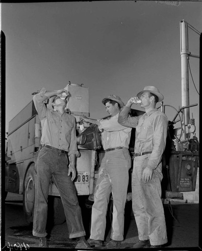 One lineman filling cup and two linemen drinking water from jug on back of line truck