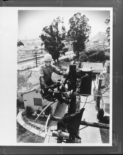 Lineman working at top of a distribution transformer pole in a residential community