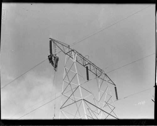 Men hanging from tower crossarm stringing conductor