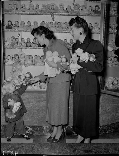 Two ladies and a little girl with two dolls at Christmas display