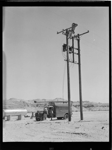 Linemen installing transformers on a pair of distribution poles in the desert