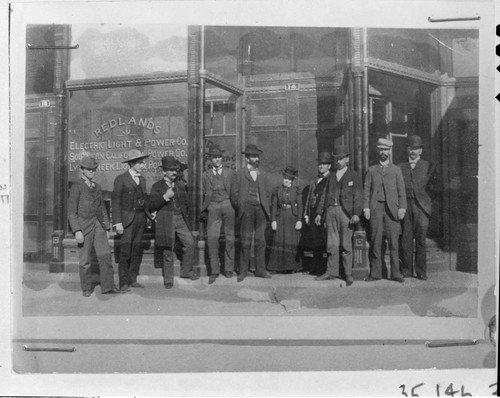 A group portrait of the officers and the office staff of the Redlands Light & Power Company standing in front of their company office on Orange Street