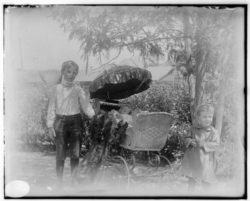 Two young boys standing next to a stroller with a baby