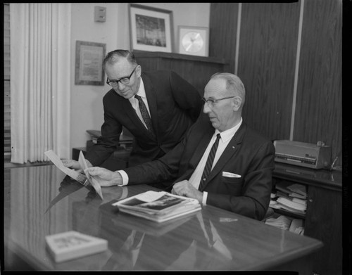 Execs. reviewing photographs and off-set portraits of both men