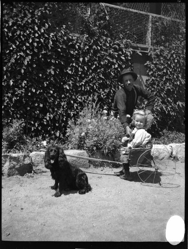 A man playing with a little girl in a cart and a dog