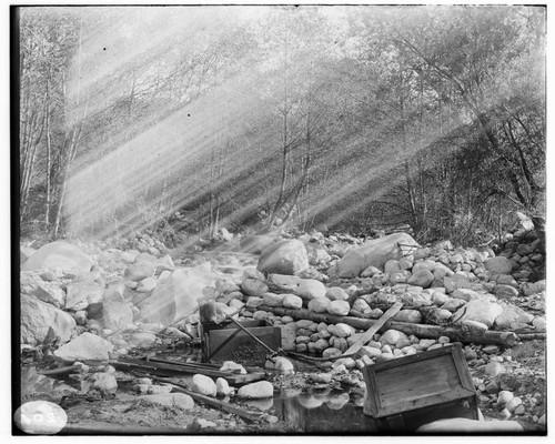 An unidentified scene showing a bed of rocks with trees in the background and small wooden boxes in the foreground