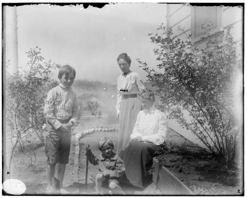 Two women and two young boys in the garden at the side of a house