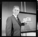 Announcer on TV-Film set speaking to camera with SCE logo over his shoulder