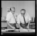 Engineer and draftsman reviewing layouts in the drafting department and manager's office