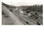 Cars at the intersection of Broadway and Landvale Road (later the intersection of Highways 24 and 13) in the Hiller Highlands district of Oakland, California. Lake Temescal and the Claremont Substation in view