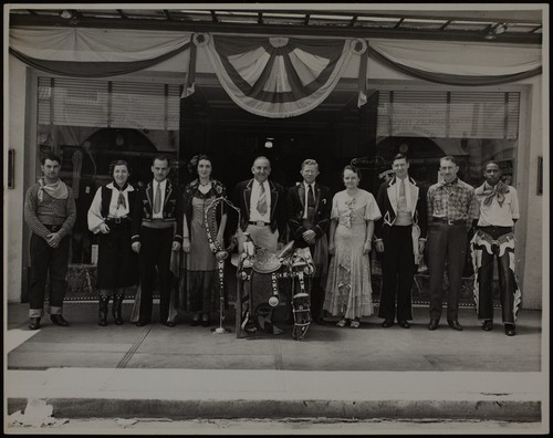 Group portrait in western garb standing in front of shop window